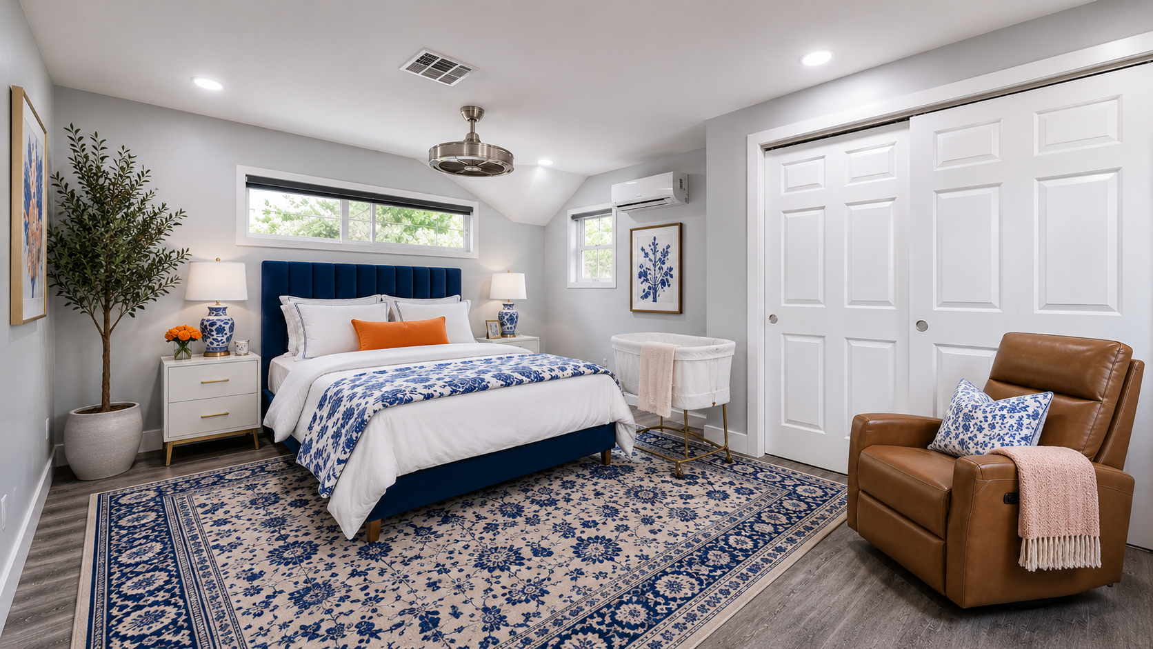 A bright suite with a navy headboard, blue and white florals, and a bassinet beside the bed